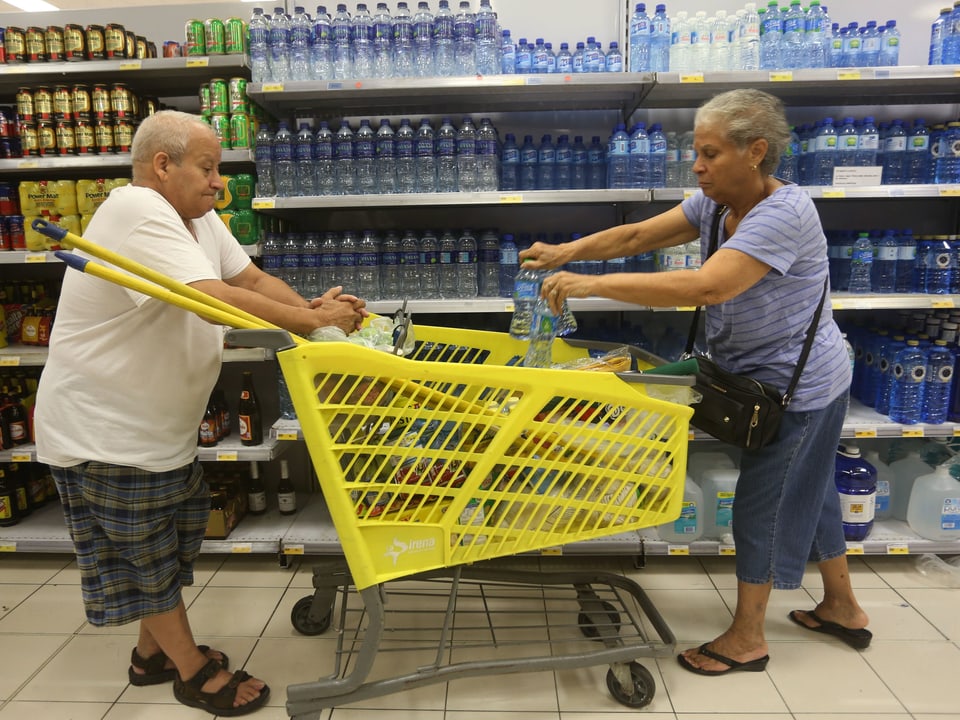 Ein älteres Paar füllen ihren Einkauftswagen mit Wasserflaschen. 