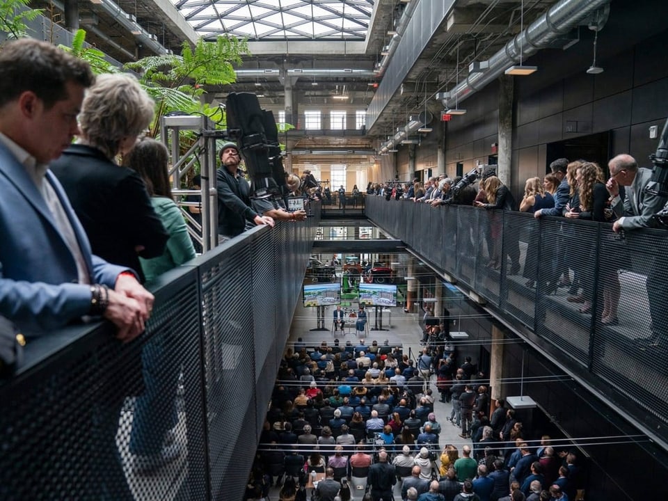 Menschen stehen auf erhöhten Galerien in einer industriellen Halle bei einer Veranstaltung.