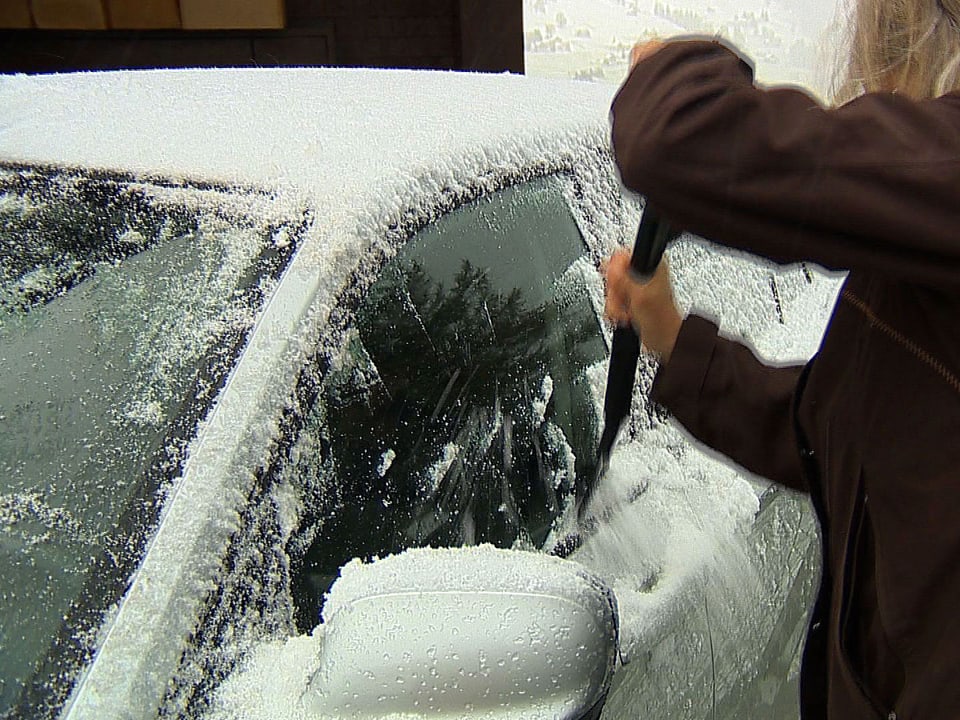 Eine Frau schabt Schnee von ihrem Auto weg.