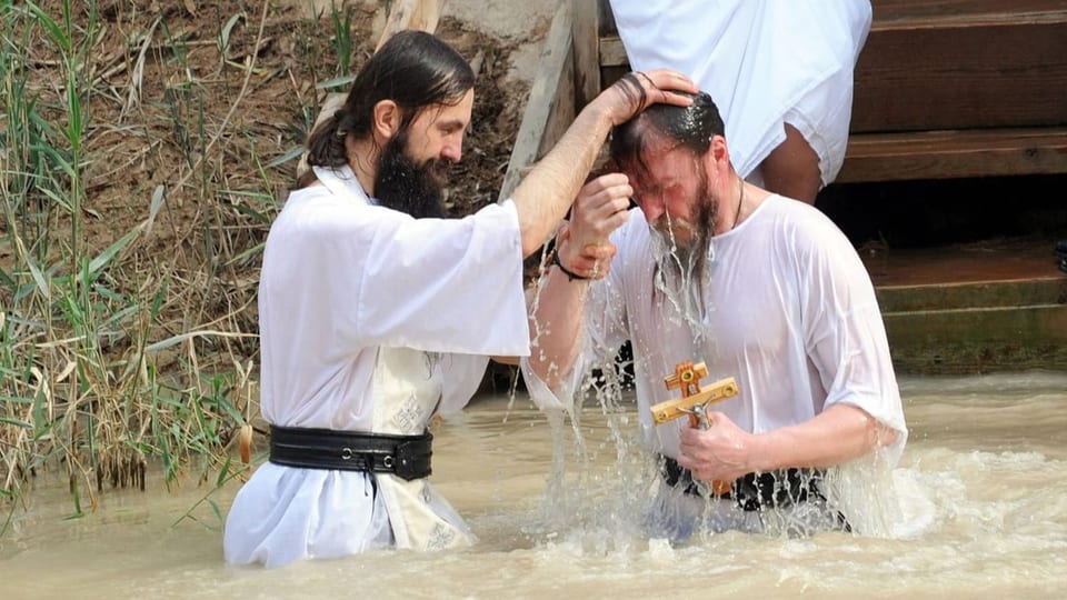 Mann mit Kreuz in der Hand lässt sich in einem Fluss taufen.
