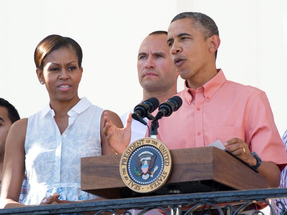 Barack Obama steht am Rednerpult, links daneben steht seine Ehefrau Michelle 