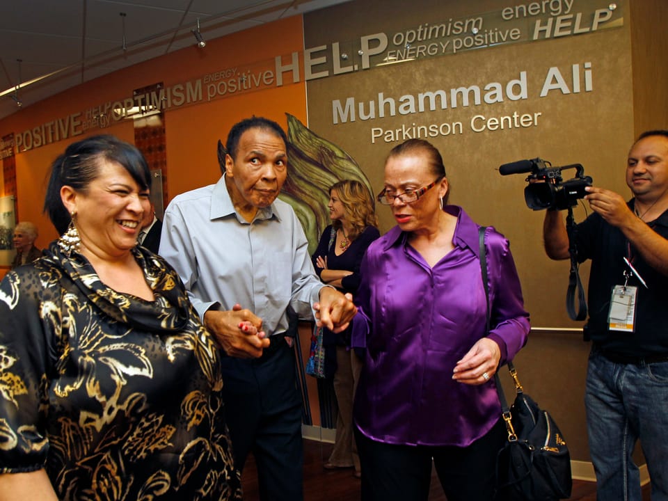 Ali  von Parkinson gekennzeichnet im Jahr 2012 bei einem öffentlichen Auftritt wird gestützt von seiner Frau und seiner Schwägerin