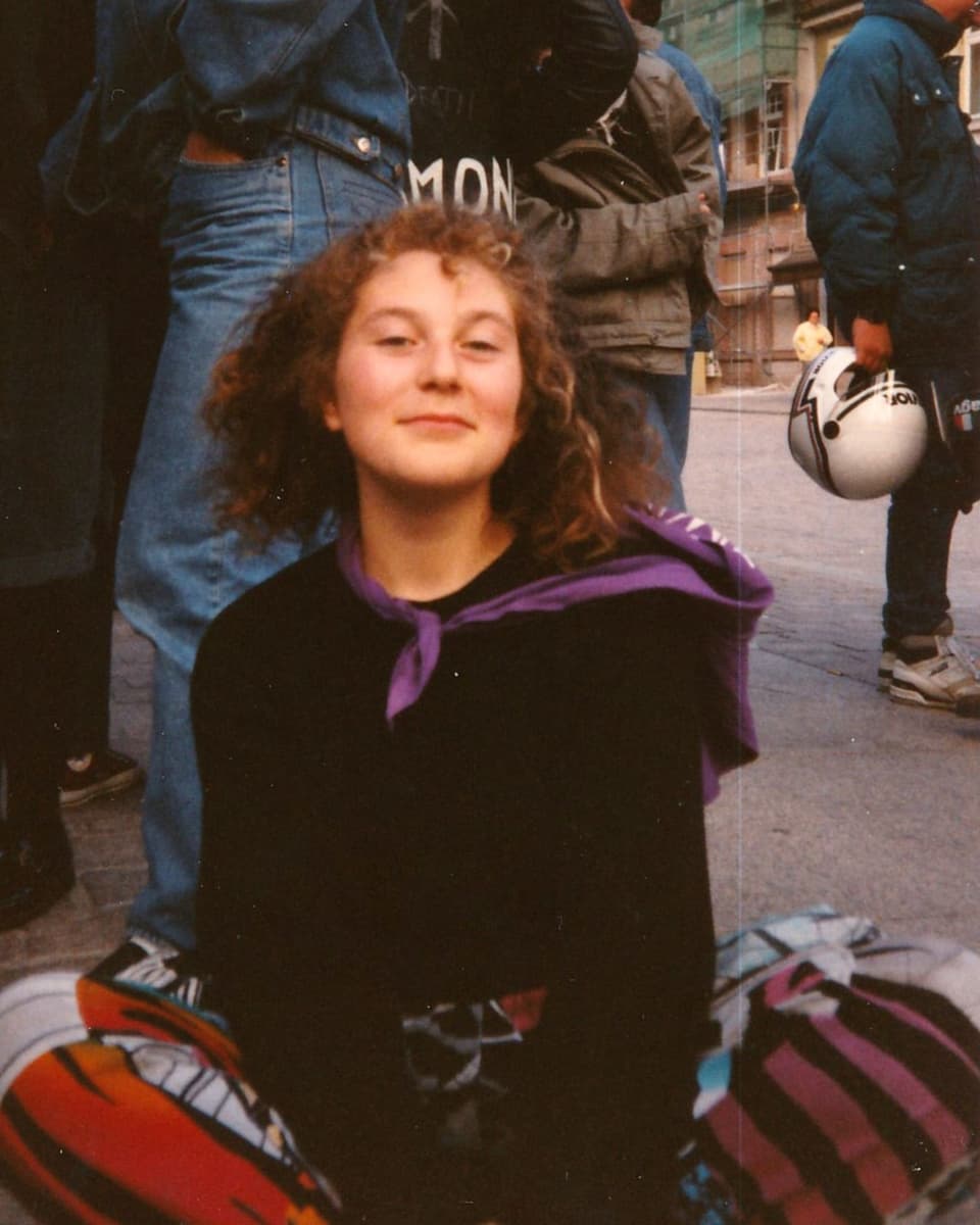Auf einem alten Foto sitzt eine Jugendliche an einer Friedensdemo auf der Strasse, um den Hans ein lila Halstuch.