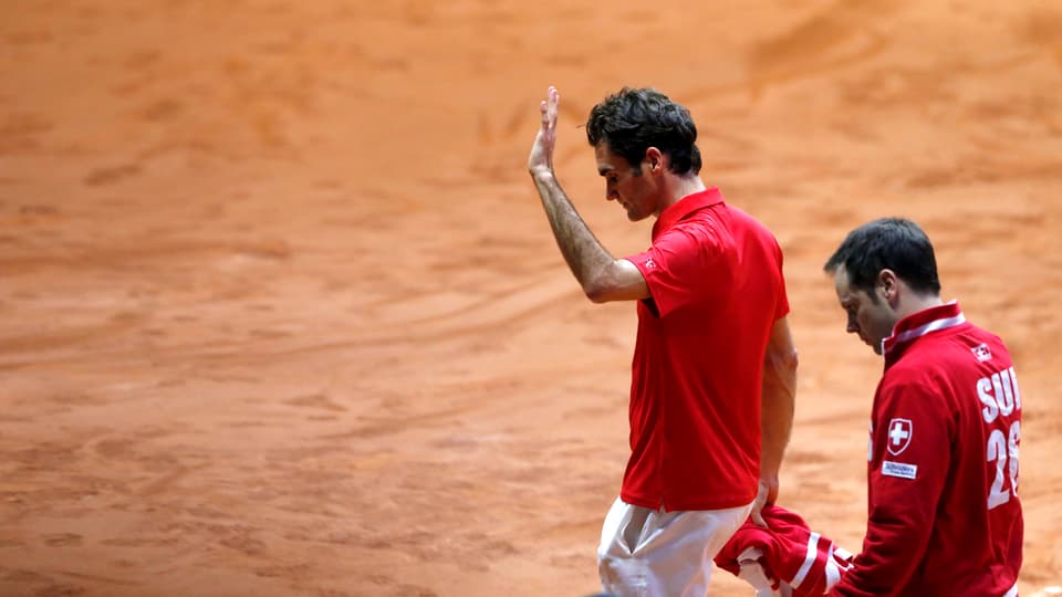 Roger Federer winkt verhalten ins Publikum und zieht mit hängendem Kopf vom Sandplatz ab. Neben ihm geht Severin Lüthi.