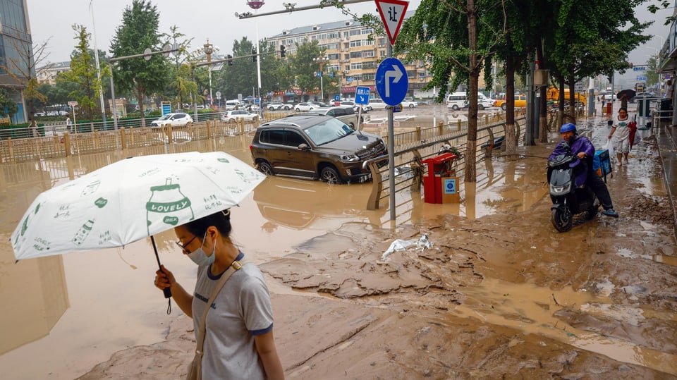 Eine Frau läuft mit hochgehaltenem Regenschirm durch die überfluteten Strassen Pekings