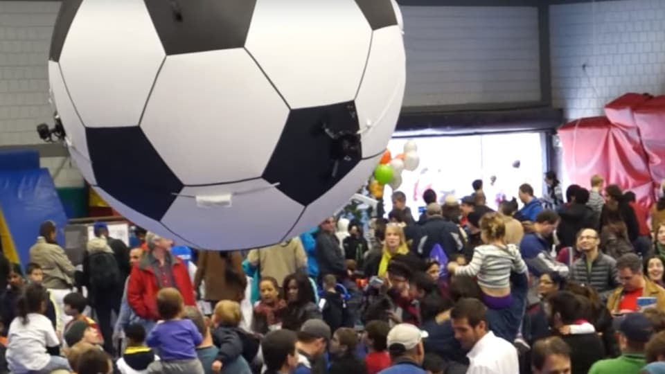 Ballon in Form eines Fussballes schwebt über einer Menschenmenge.