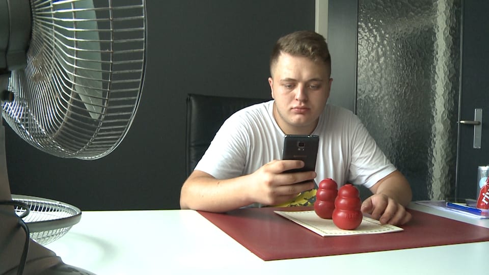 Ein junger Mann sitzt an einem Tisch und bedient sein Handy.