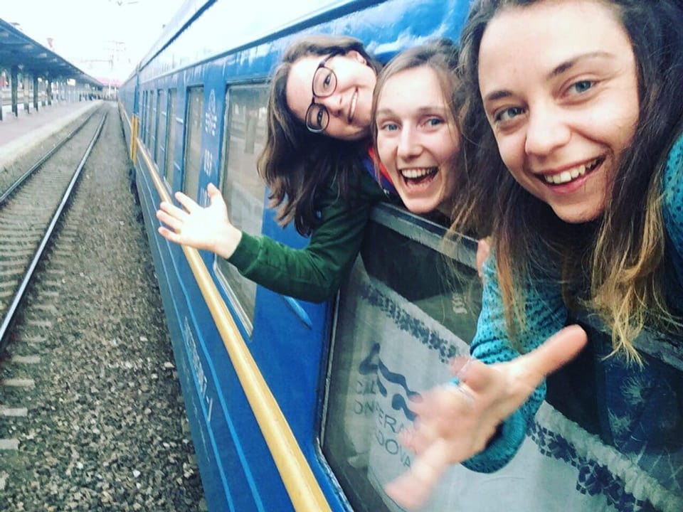 Drei junge Frauen lachen und winken aus dem Zug raus.