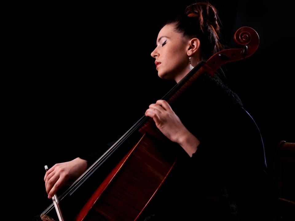 Eine Frau mit hochgebundenen, braunen Haaren spielt Cello. Sie hat ihre Augen geschlossen.