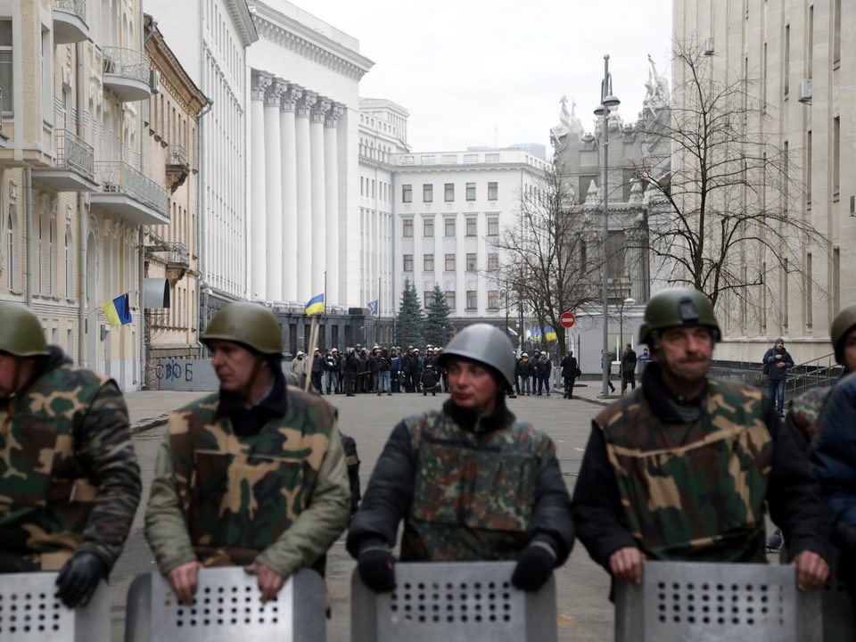 Eine Reihe Aktivisten in Militärkleidung umzingelt das Paralementsgebäude in Kiew. 