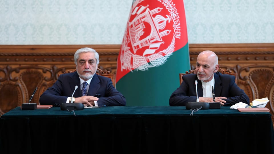 Abdullah und Ghani an einem Tisch vor einer Afghanistan-Flagge.