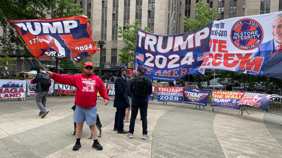 Mehrere Personen vor Trump 2024-Bannern in einer Stadt.