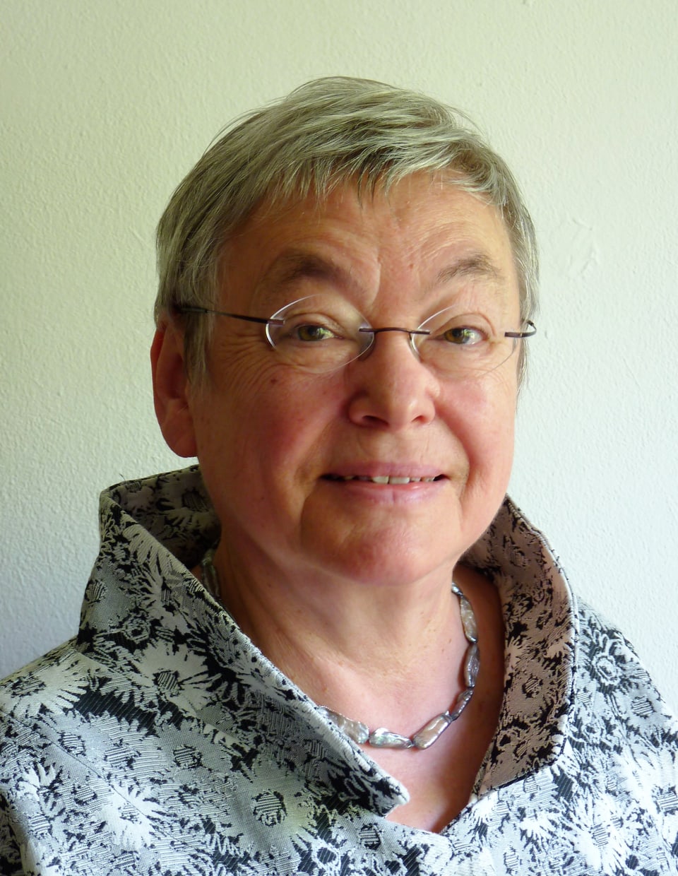 Eine ältere Frau mit kurzen, grauen Haaren und Brille. 