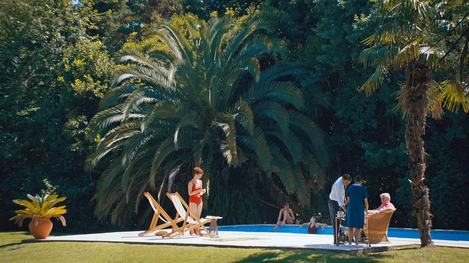 ein Pool mit vielem Palmen und Menschen, die sich sonnen