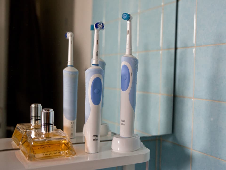 Zei elektrische Zahnbürsten neben einem Parfümflacon vor einem Badezimmerspiegel