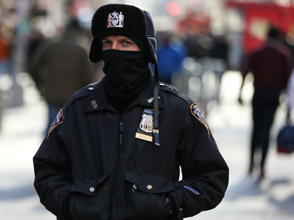 Polizist mit Mütze und Schal vor dem Mund.