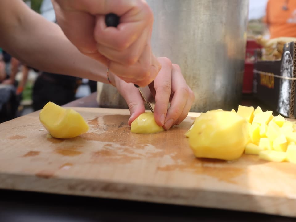 Hände haben ein Messer in der Hand und schneiden Kartoffeln.