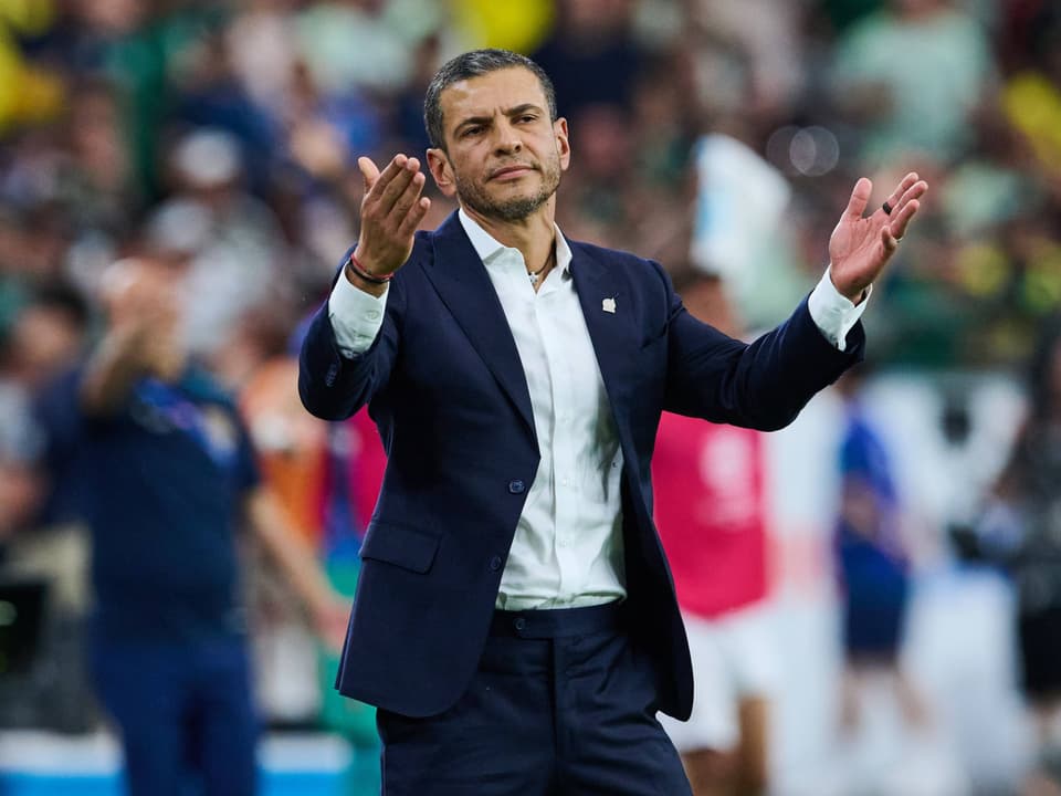 Man in suit gesturing at sports field.