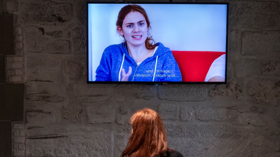 Eine Frau sitzt vor einem Bildschirm, auf dem eine andere Frau zu sehen ist.