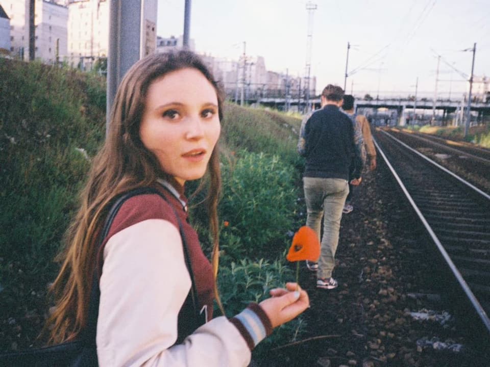 Frau am Bahngleis mit einer Blume in der Hand.