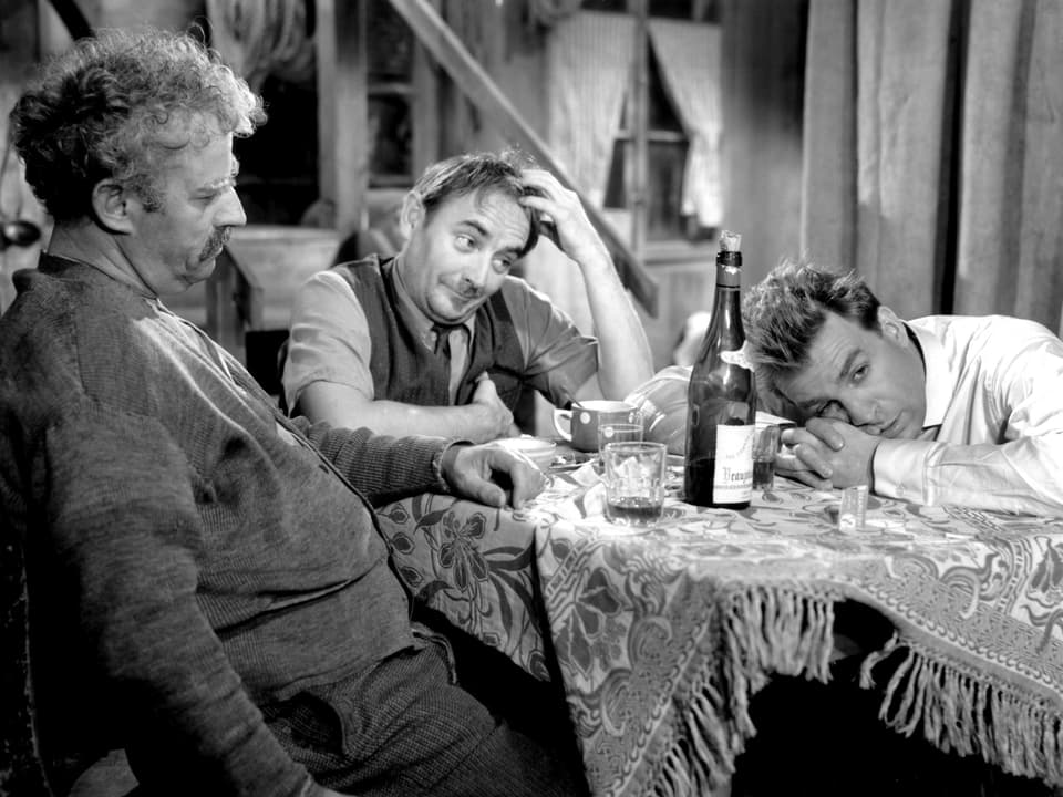 Drei Männer sitzen an einem Tisch und trinken wein.