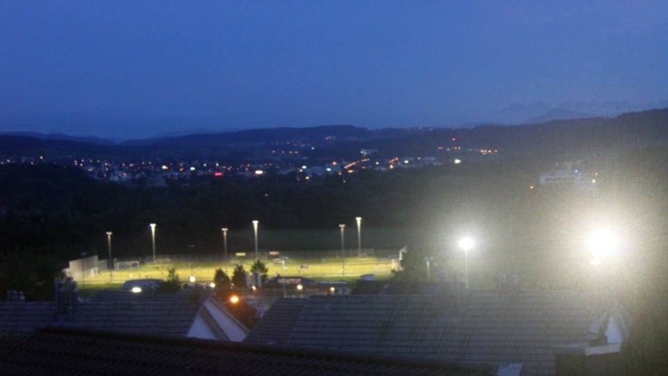 Ein Sportplatz bei Dunkelheit: links gut ausgeleuchtet aber blendfrei – rechts den Betrachter stark blendend.