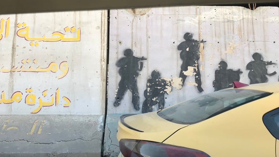 Graffiti an einer Sicherheitsmauer in Bagdad, das bewaffnete Personen zeigt