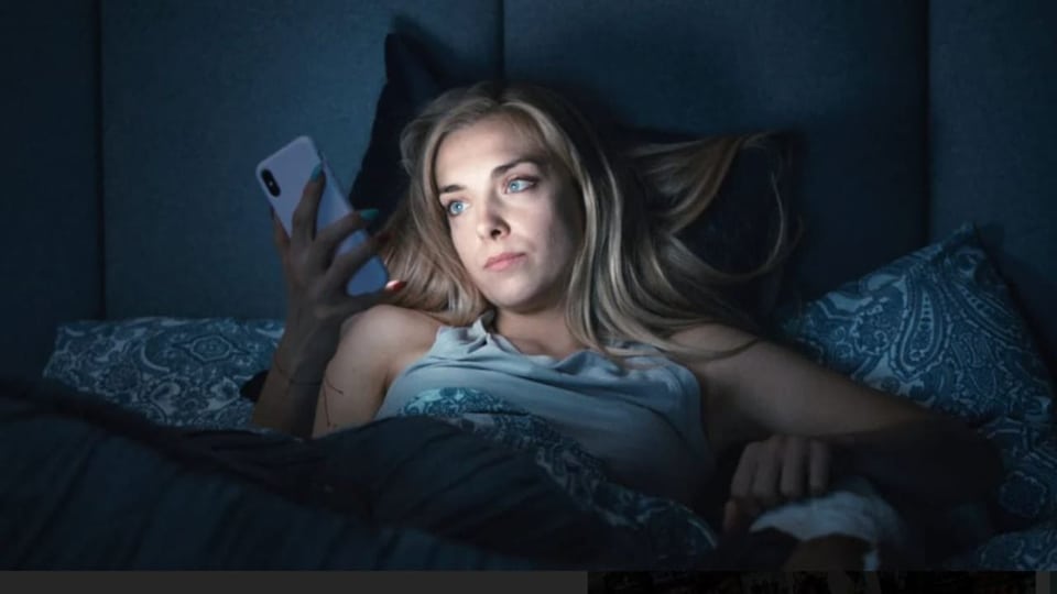 Frau liegt im Bett und schaut aufs Handy 