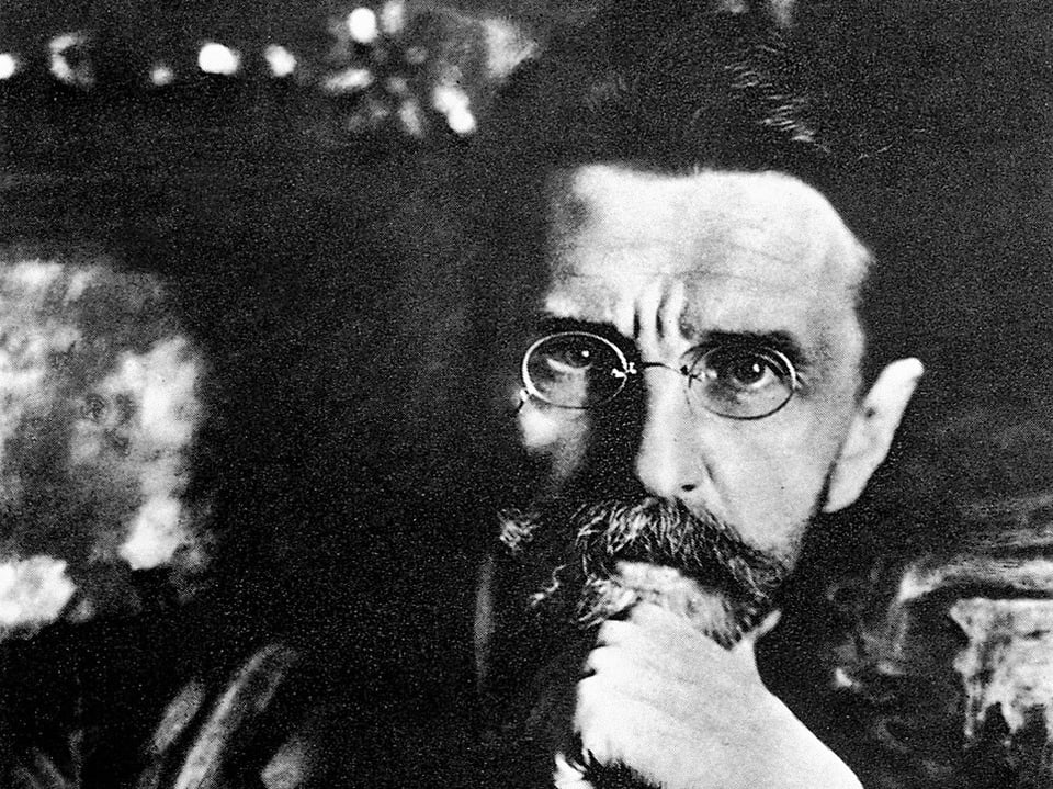 Portrait of a middle-aged man propping his chin. He is thin, has whiskers and wears glasses.