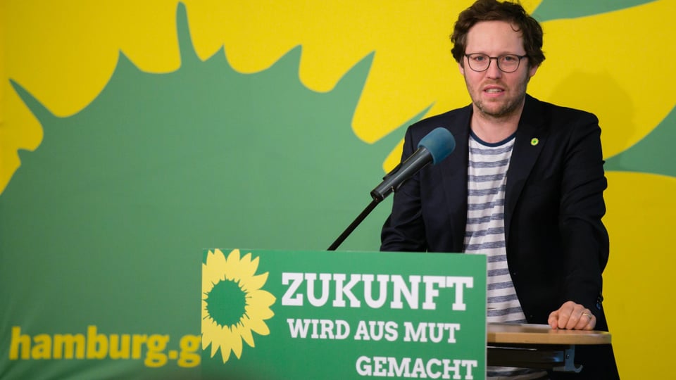Mann mit Brille an einem Rednerpult, Dahinter das Grünen-Logo.
