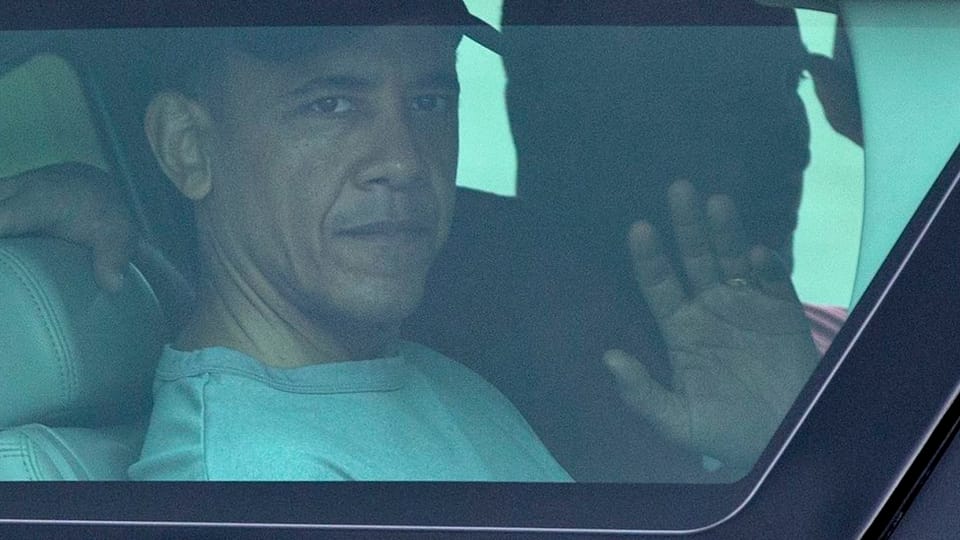 Obama mit ernster Miene winkt aus einem Autofenster.