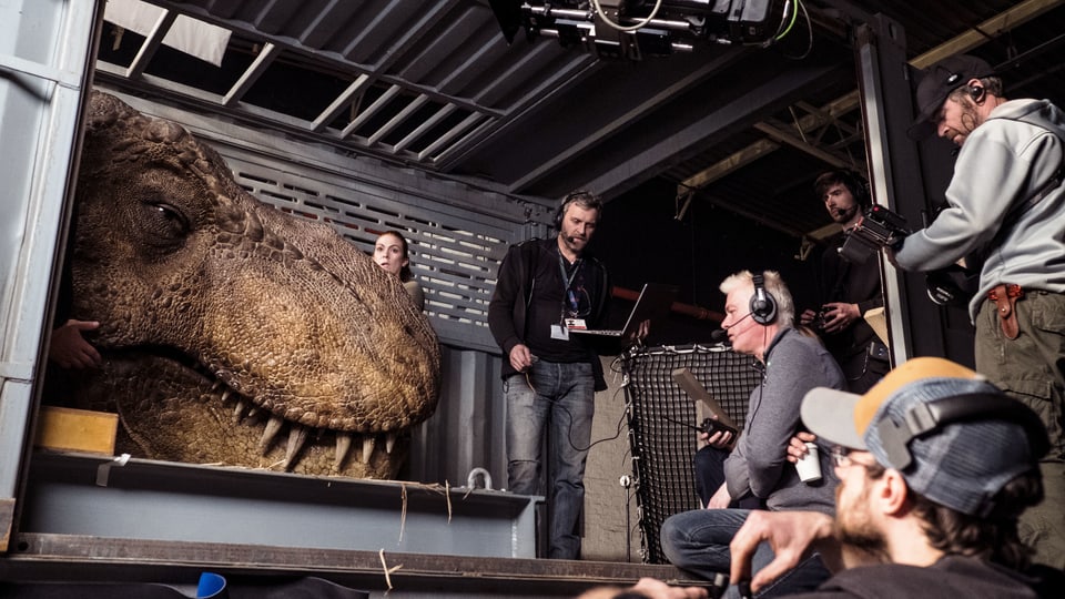 Filmset, vielen Menschen stehen um einen riesigen künstlichen Dinosaurier-Kopf