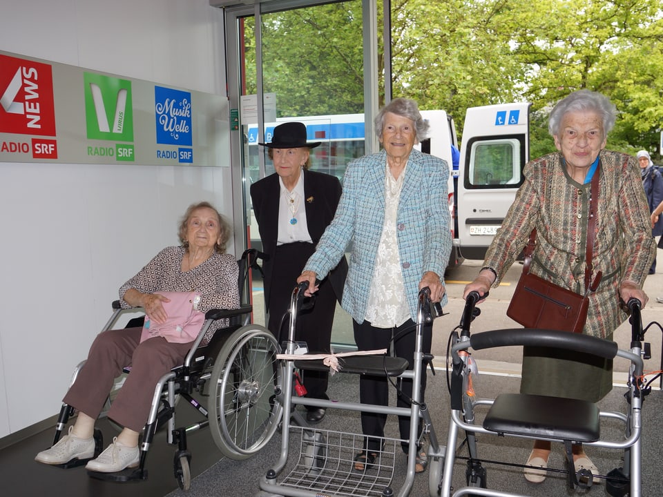 vier Damen mit Rollatoren, Gehstöcken und im Rollstuhl.