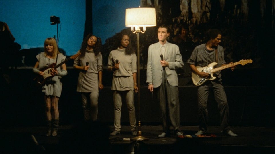 Die Band «Talking Heads» steht auf einer spärlich beleuchteten Bühne und performt.