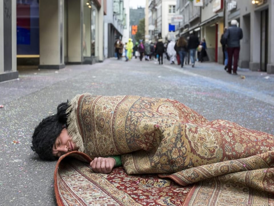 Ein Fasnächtler schläft eingerollt in einen Teppich mitten in der Luzerner Altstadt.