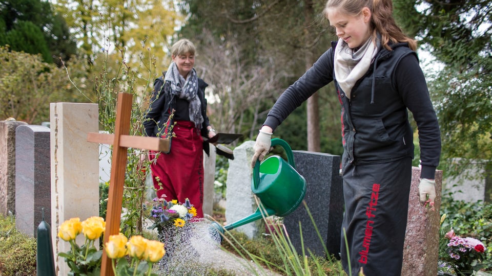 Frau giesst Blumen auf Friedhof