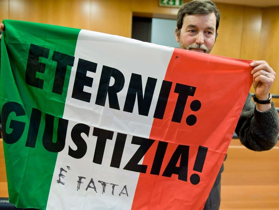 Mann hält italienische Flagge mit der Aufschrift «Eternit: Giustizia» in die Kamera