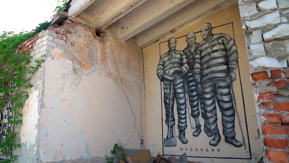 Graffiti von drei Häftlingen an einer zerfallenen Hauswand 