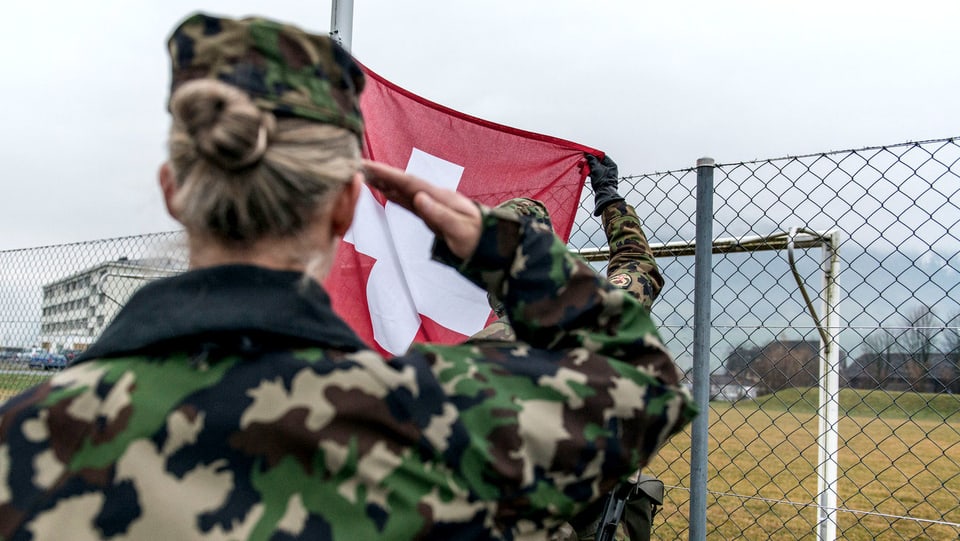 Eine Frau salutiert vor einer Schweizer Flagge