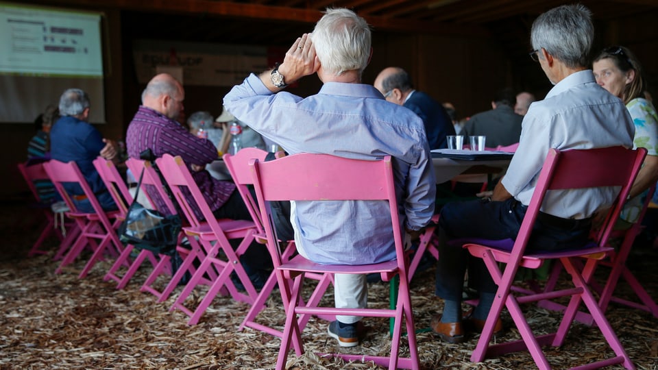 Mehrere Delegierte sitzen auf Stühlen in einem Bauernhof.