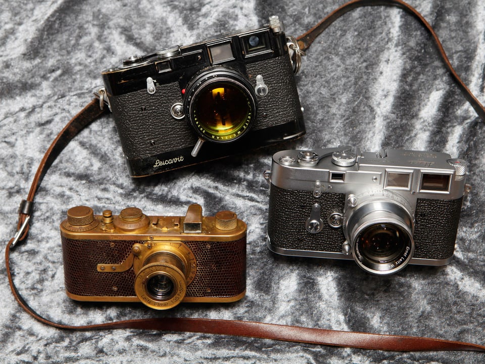 Drei alte Leica-Modelle auf silbernem Grund.