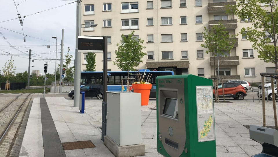Eine Tramhaltestelle mit Billettautomat, im Hintergrund ein blauer Bus