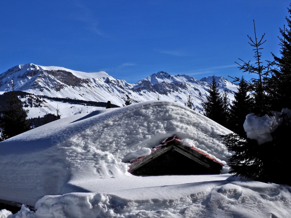 Meterhoch Schnee auf einem Hausdach, darüber blauer Himmel.