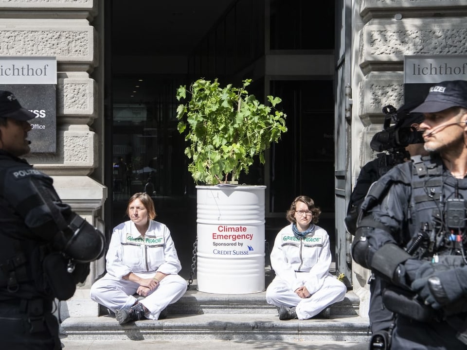 Frauen sitzen mit einem Bäumchen vor Eingang der Credit Suisse