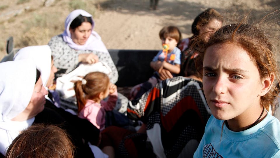 Flüchtlingsmädchen auf einem Traktor. Dahinter Frauen und Kinder.