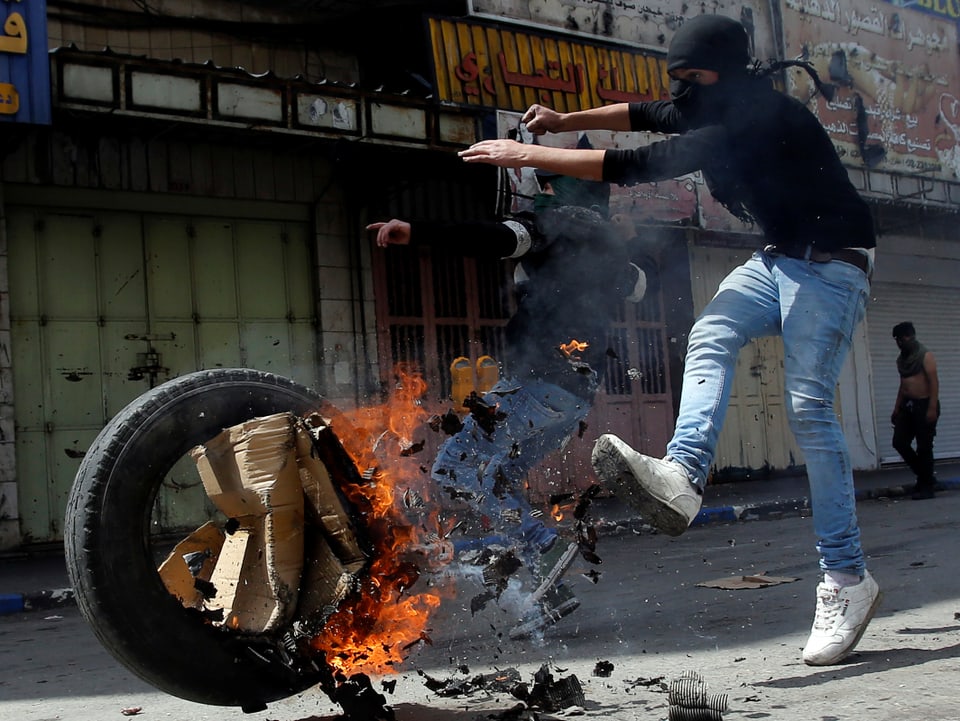 Junger Palästinenser stösst einen brennenden Reifen mit dem Fuss weg.
