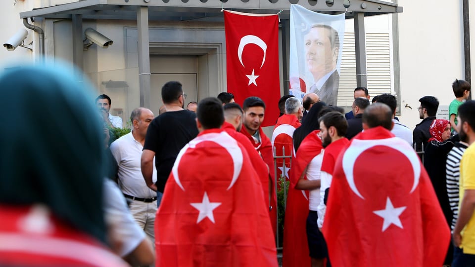 Mehrere Personen, von hinten fotografiert, viele haben eine türkische Fahnen über ihren Schultern.