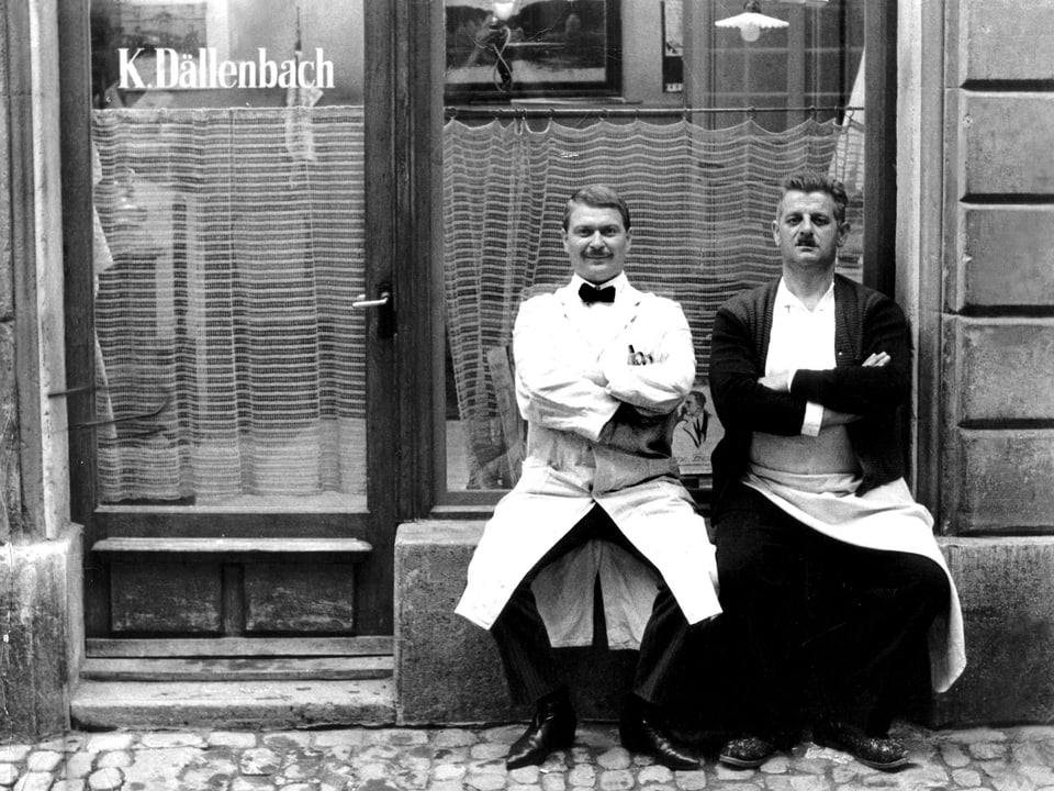 Zwei Männer sitzen vor einem Friseurgeschäft.