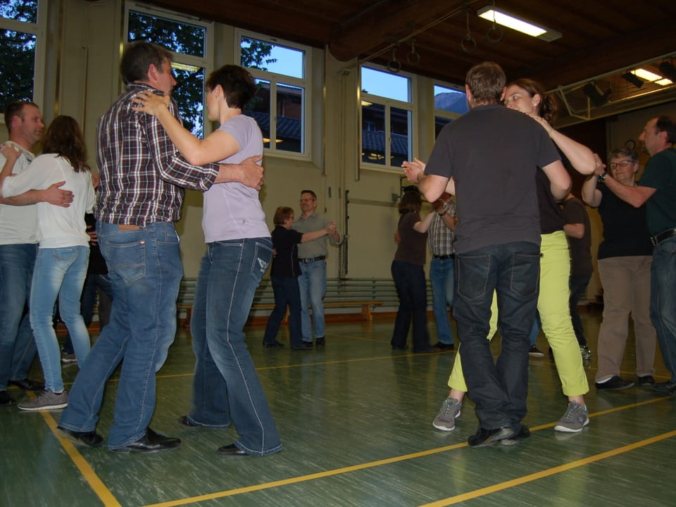 Mehrere Tanzpaare tanzen in einer Turnhalle im Kreis.