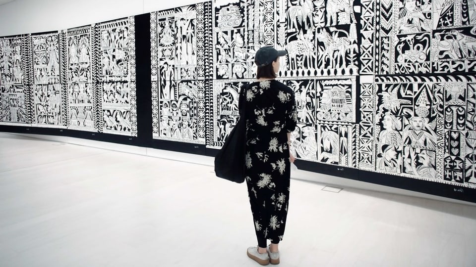Frau in schwarz-weissem Klein steht vor schwarz-weissem Kunstwerk.